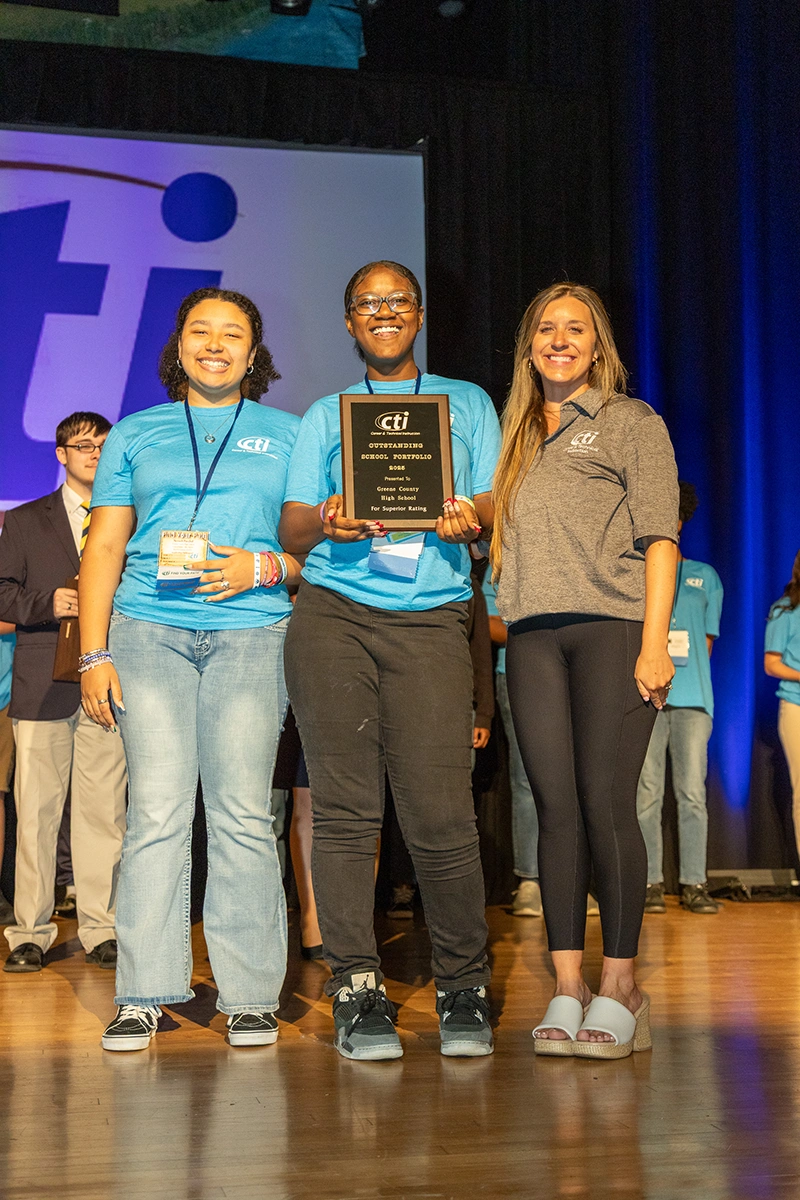 two female students in blue shirts receiving an award on stage from a female adult